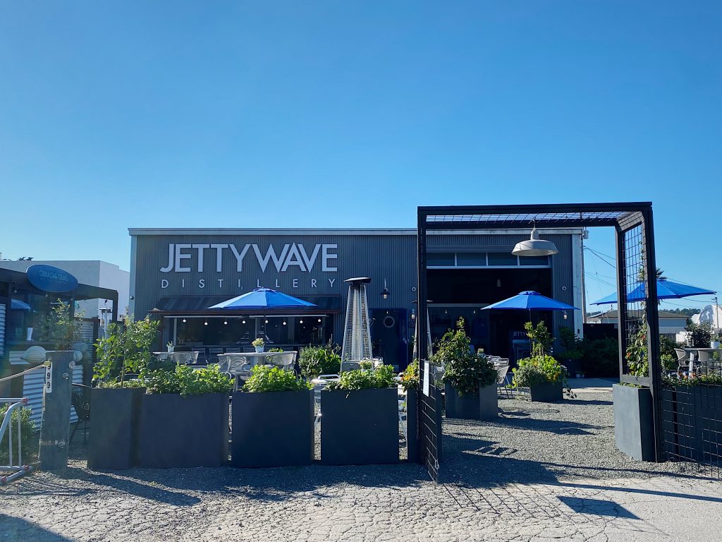 An industrial style building with the Jettywave Distillery sign and an outdoor dining area in front with plenty of planter boxes.
